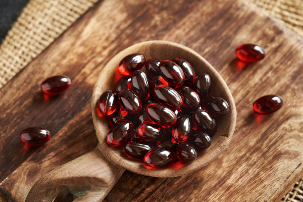 Close-up of glossy red krill oil capsules in a wooden bowl on a textured wooden board. The setting conveys a natural, health-focused theme with earthy tones.