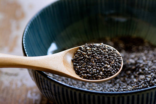 A wooden spoon holds a scoop of black chia seeds above a dark blue bowl filled with more seeds, creating a natural and wholesome ambience.