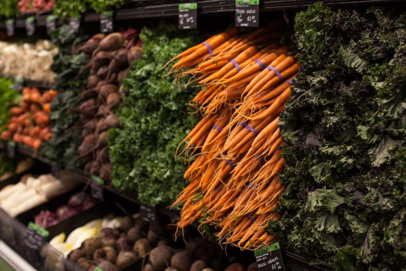 Fresh whole vegetables including carrots, beets, and kale displayed at a grocery market