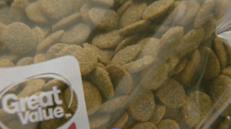 Close-up of dry dog food in a clear plastic bag with a "Great Value" label. The kibble is brown and disc-shaped, conveying a casual, effortless feel.