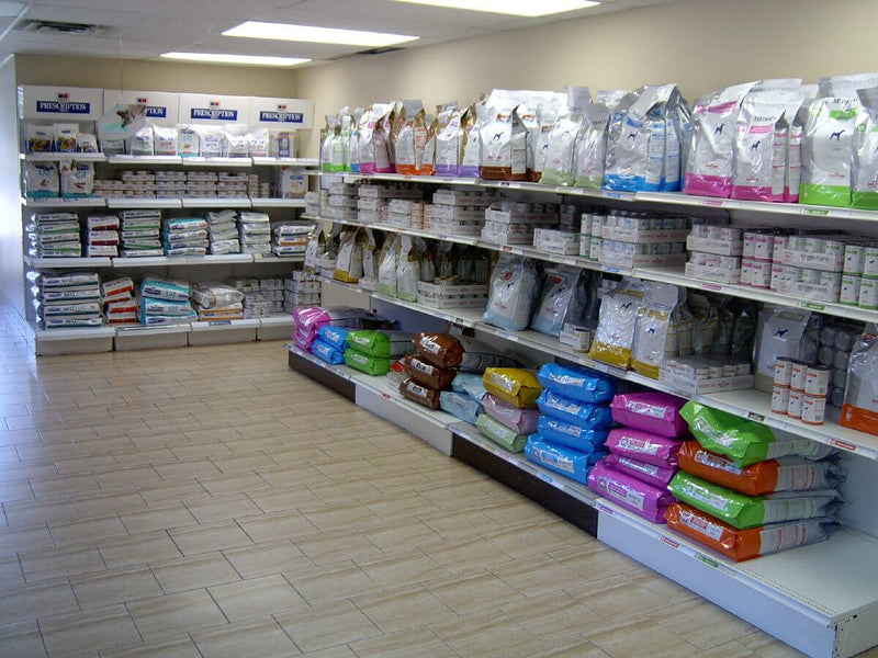 Shelves filled with colorful bags and cans of pet food line the walls of a well-lit store with tiled floors, creating an organized and inviting atmosphere.