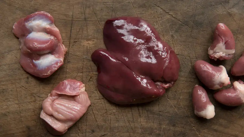Assorted raw organ meats including liver and kidney displayed on a wooden cutting board, illustrating nutrient-dense by-products used in dog food
