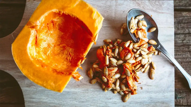 Halved pumpkin on a wooden cutting board with seeds and a spoon beside it