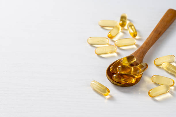 Wooden spoon holding several golden gel capsules, scattered on a white surface. The image conveys a sense of health and wellness.