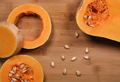 Slices of butternut squash with seeds scattered on a wooden board. The squash’s vibrant orange flesh contrasts with the neutral wood, creating a fresh and natural feel.